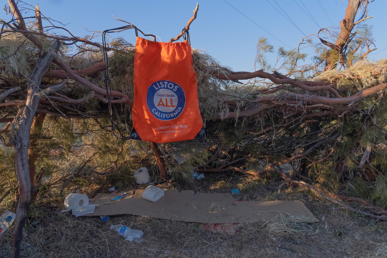 A photo of a hut made of sticks and branches with a bag from Listos California hanging