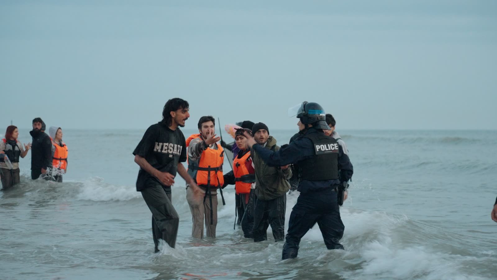 A migrant confronts a French police officer in the surf as a boat to Britain loads.
