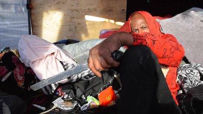 A photo of a man holding a home made sword inside a skid row tent